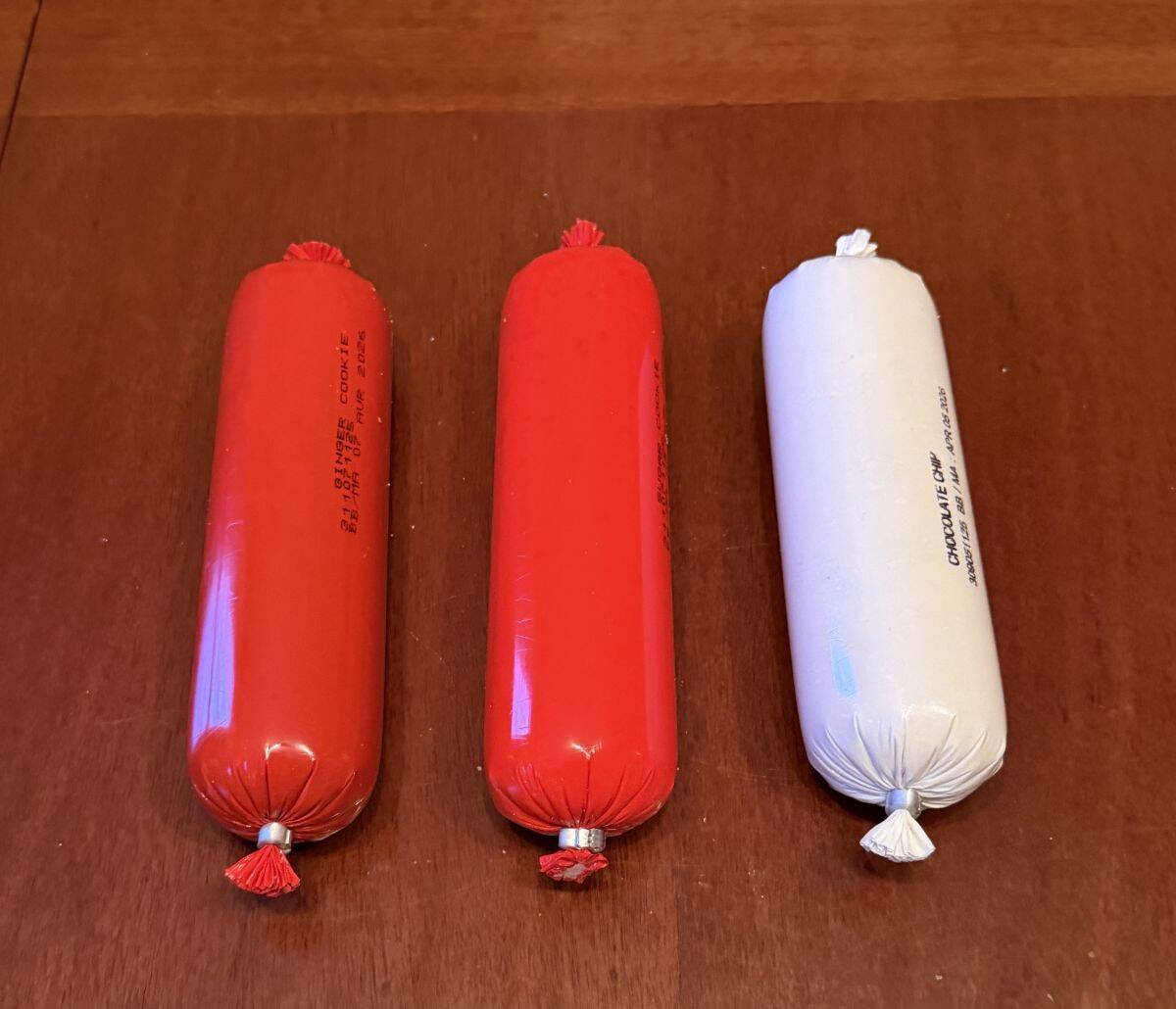 Image of three rolls of cookie dough sealed and sitting on a white table.