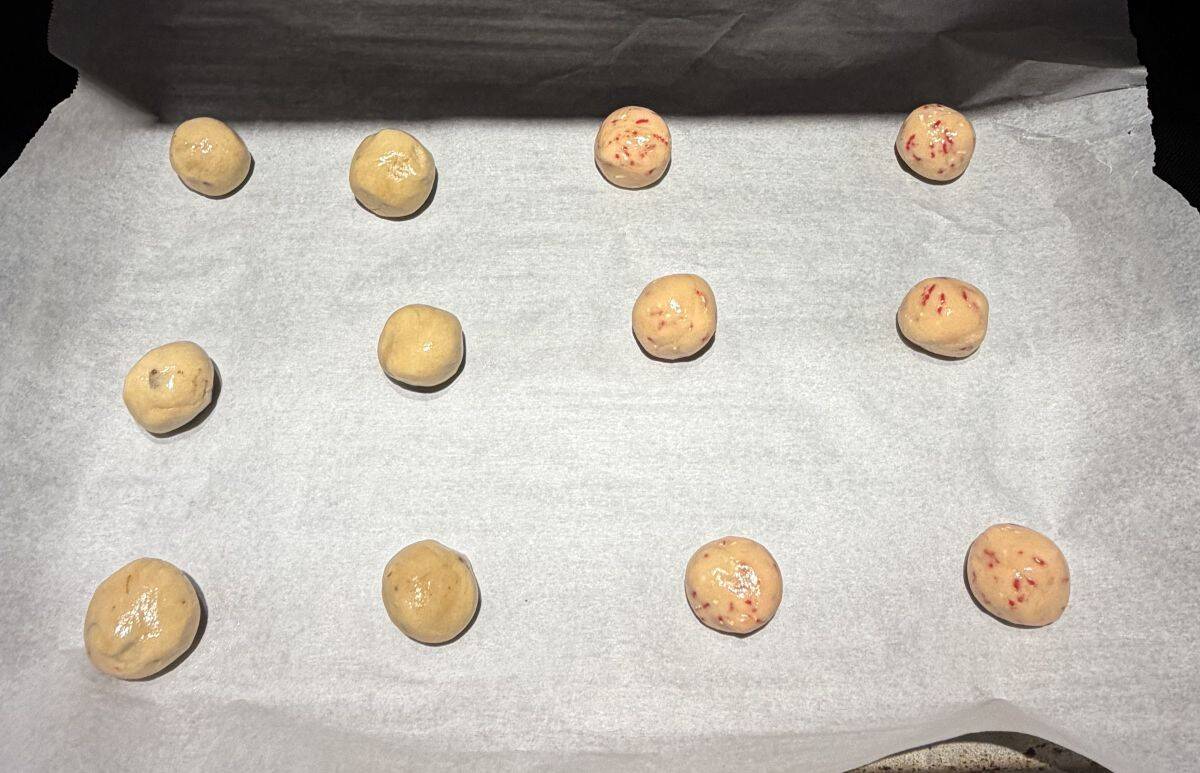 Image of a parchment paper lined baking tray with cookie dough balls on it.