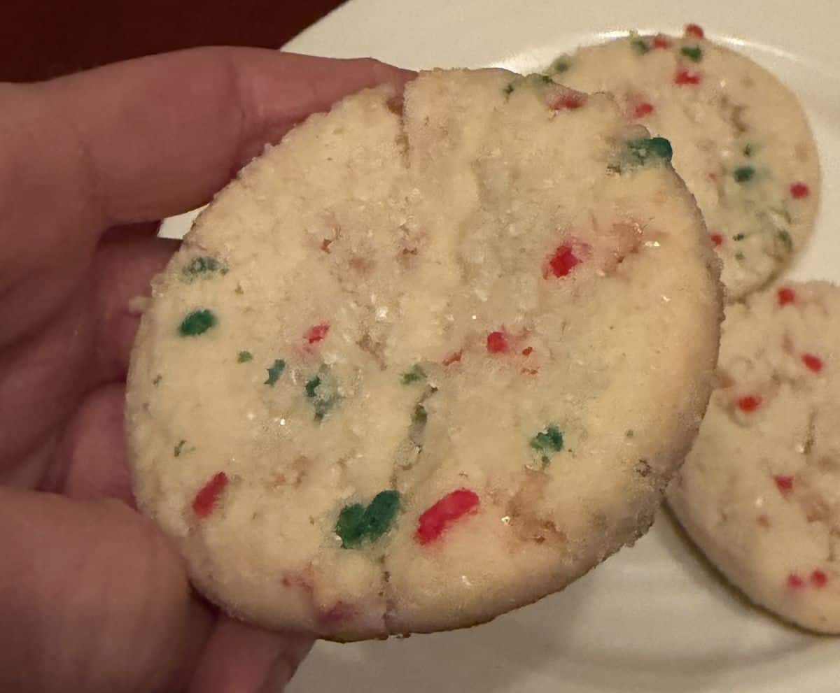 Closeup image of a hand holding one toffee shortbread cookie close to the camera so you see the sprinkles and sugar on top. 