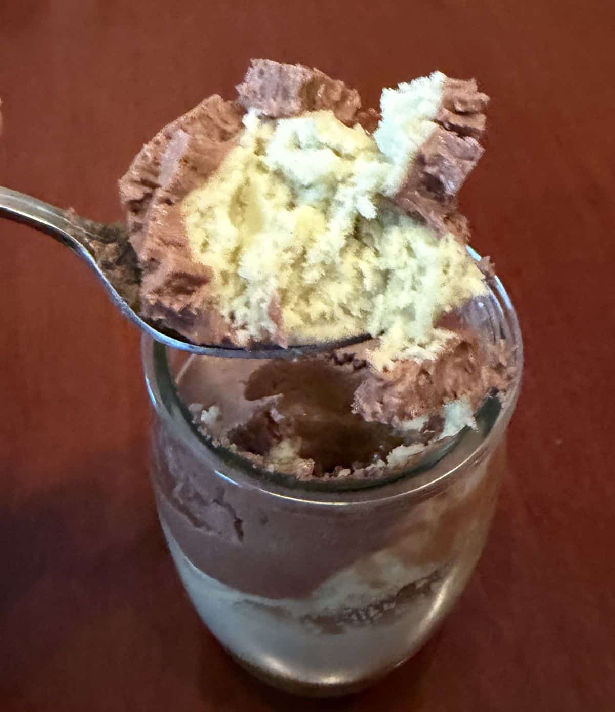 Image of a spoon hovering over the Delici dessert with pistachio cream and chocolate on it.