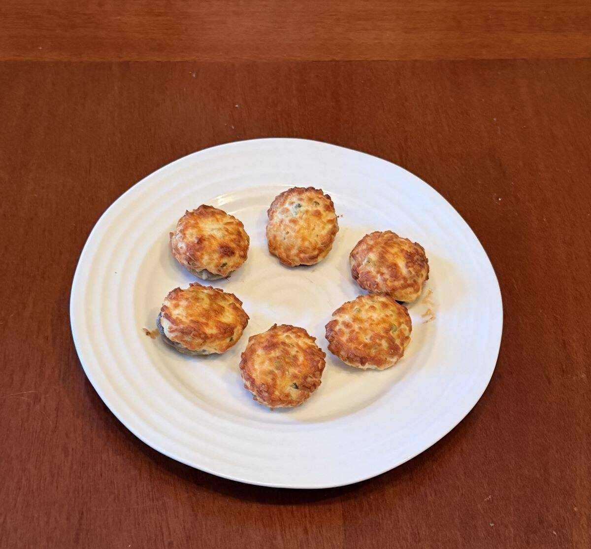 SIx stuffed mushrooms with golden crisp tops served on a white plate.