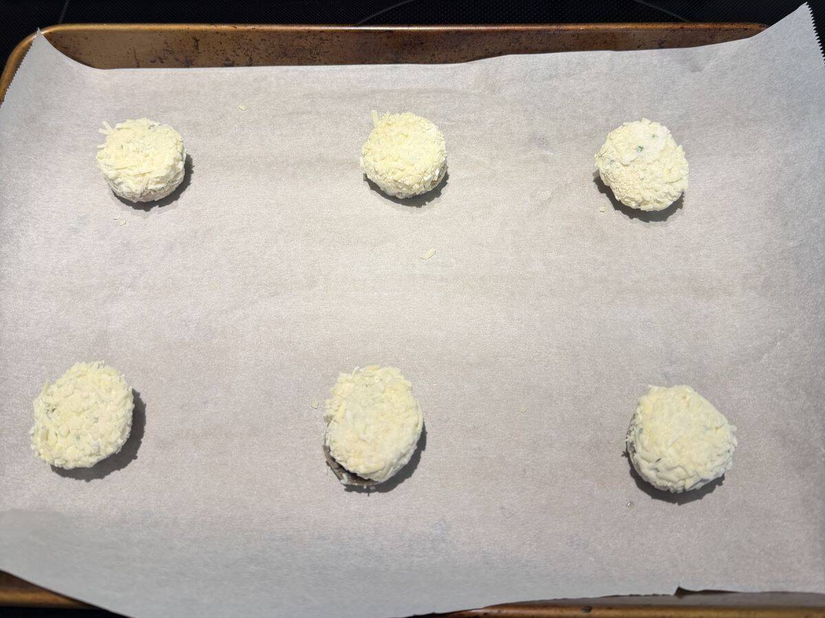 Image of six frozen stuffed mushrooms on a parchment paper lined baking tray before being cooked.