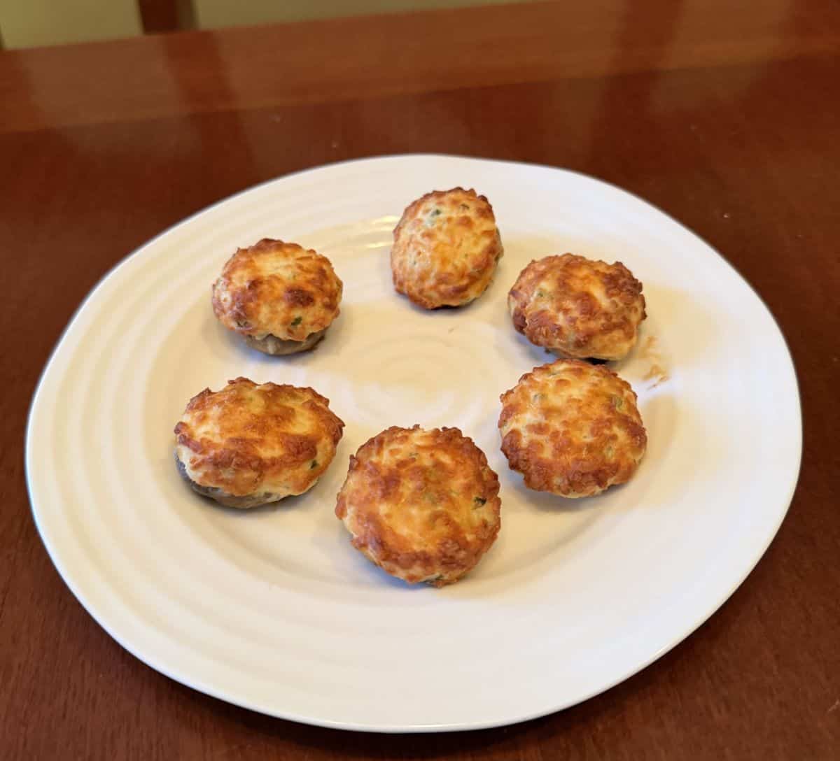Image of six stuffed mushrooms cooked and served on a white plate.