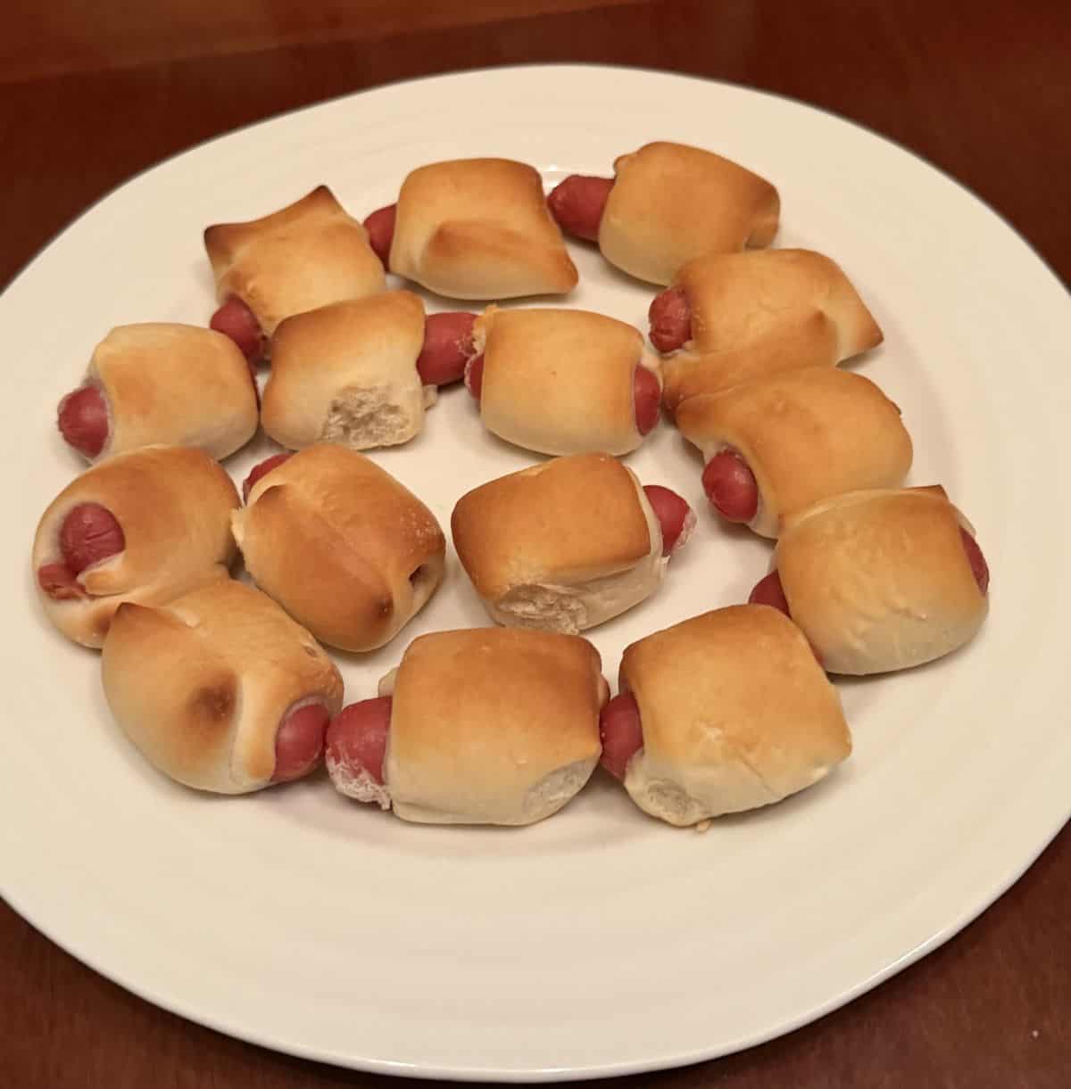 Image of fifteen baked mini sausages served on a white plate.