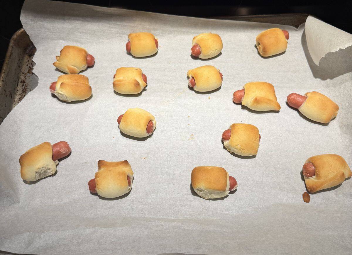 Image of the mini sausages on a parchment lined baking tray after coming out of the oven.