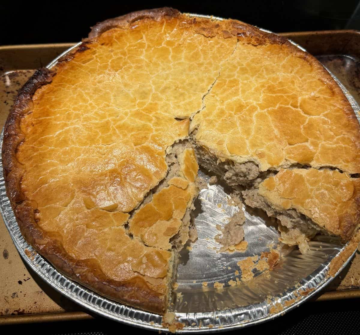 Image of the tourtière sitting on a stove top with a slice taken out of it so you can see the inside.