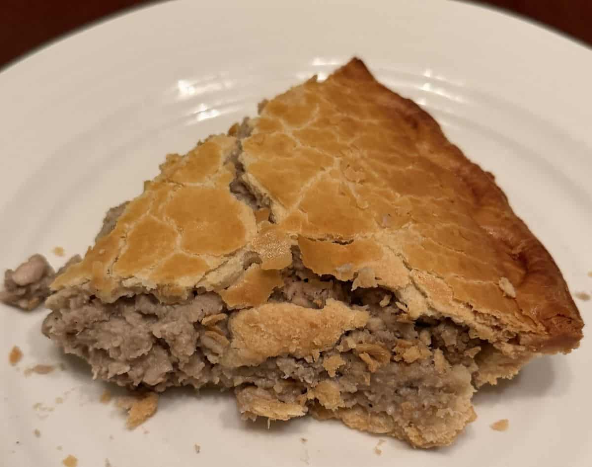 Side view image of one slice of meat pie served on a white plate so you can see the filling.