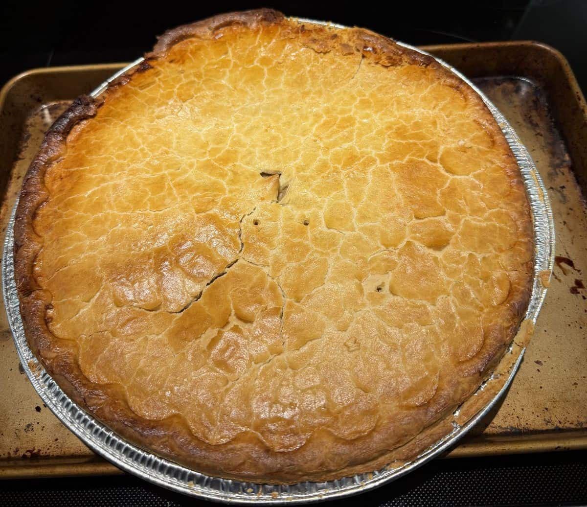 Top down image of one cooked tourtière sitting on a cookie sheet on top of an oven.