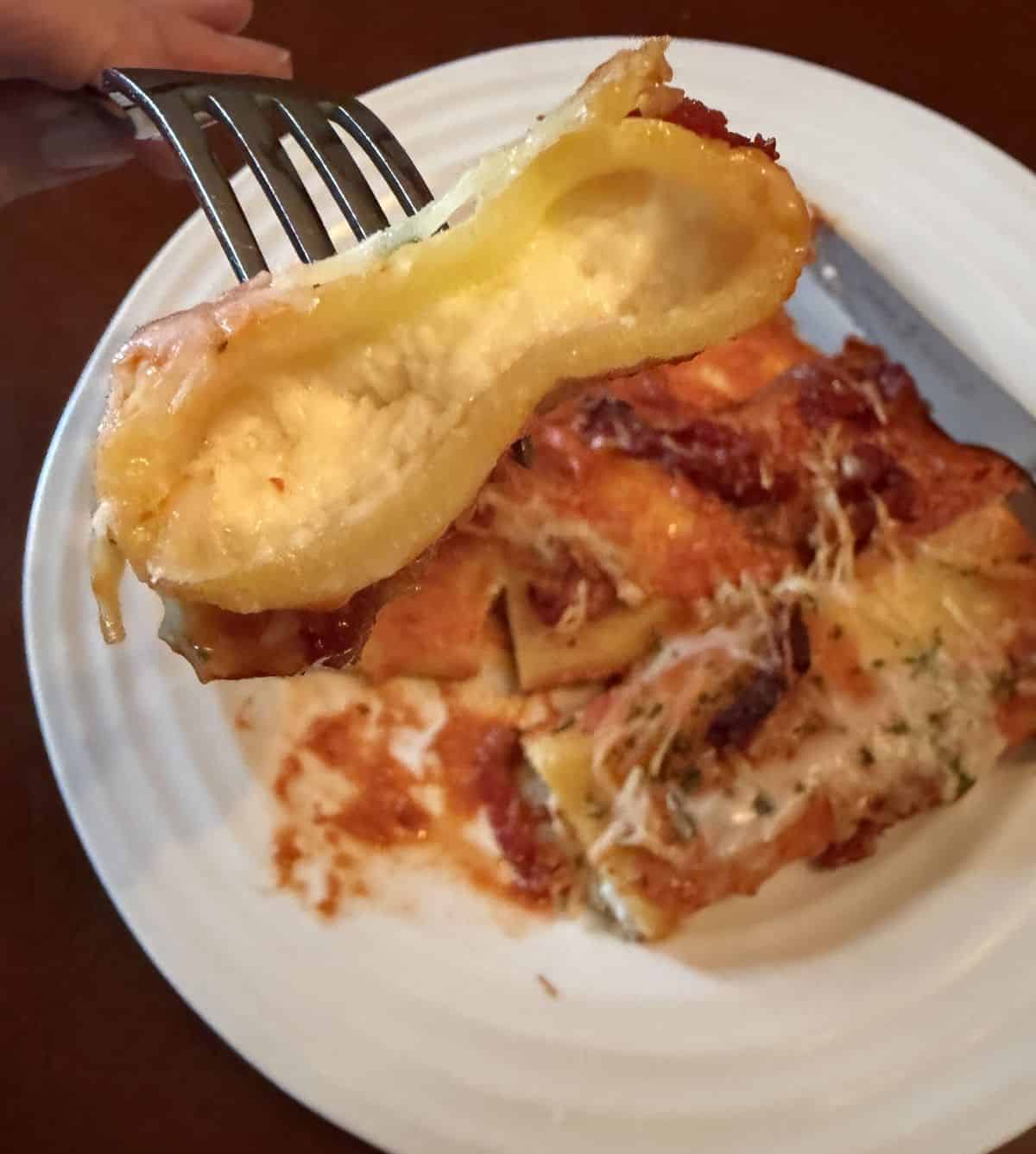 Image if a fork with a piece of manicotti on it so you can see the filling hovering over a plate of manicotti.