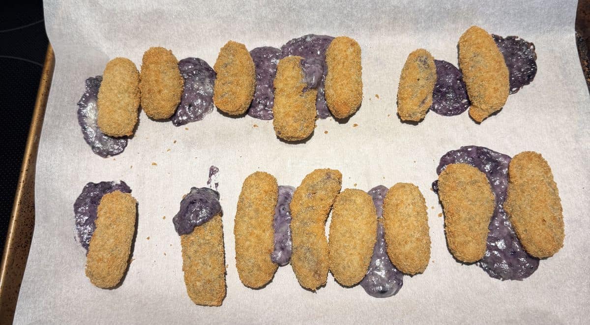 Image of cooked blueberry & brie bites on a parchment lined baking sheet. The bites have filling coming out of them.