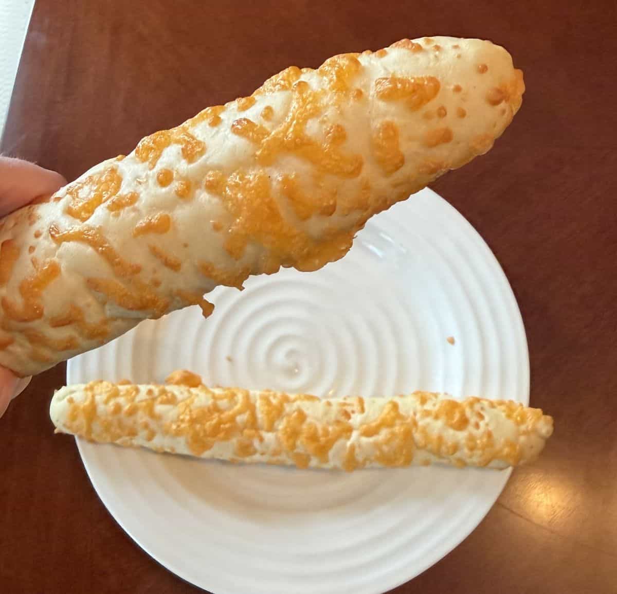 Image of a hand holding one cheesy bread stick up close to the camera.