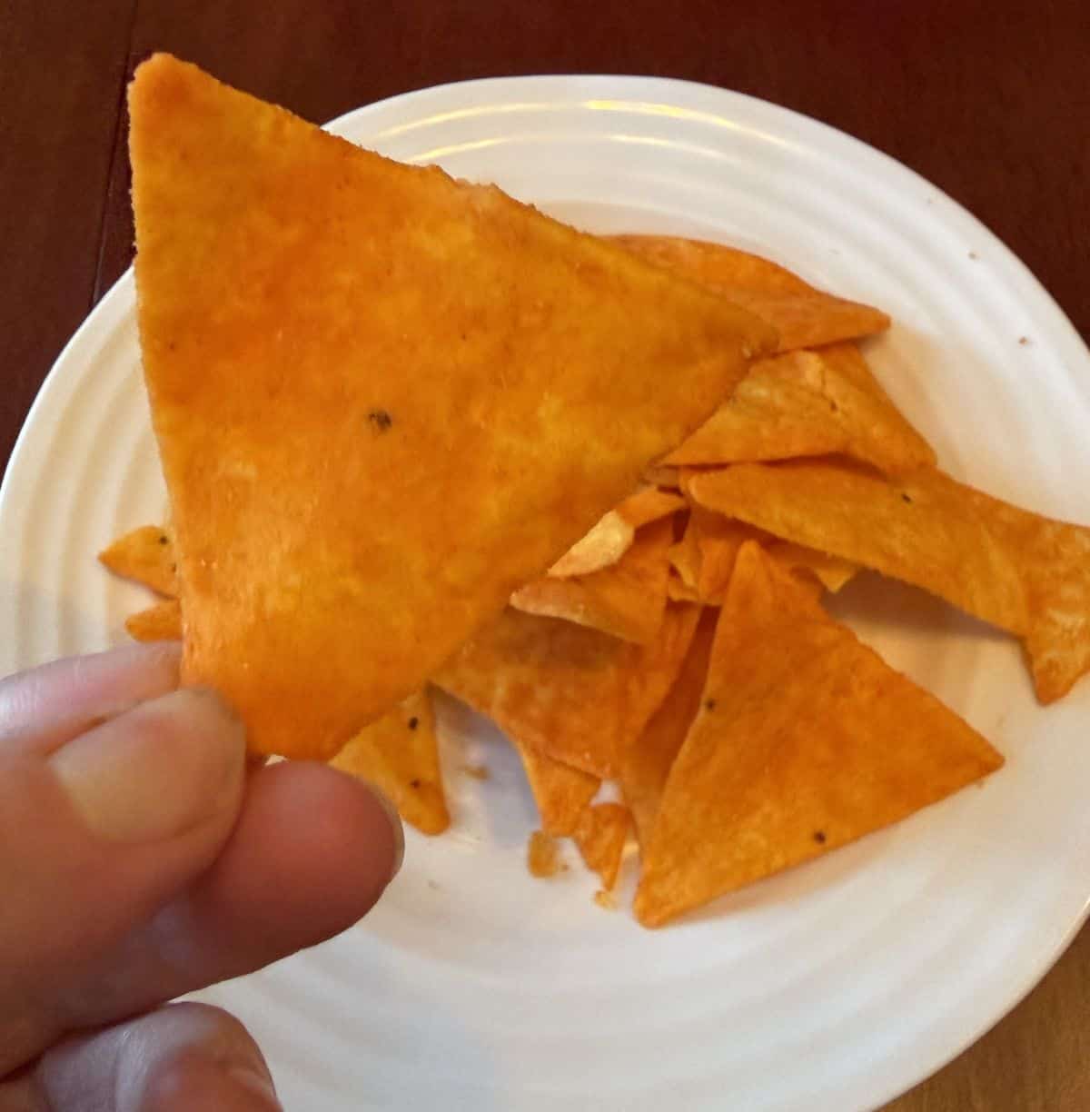 Image of a hand holding one nacho cheese chip close to the camera.
