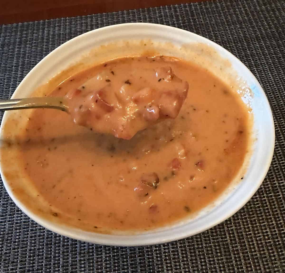 Image of a bowl of roasted red pepper & gouda soup with a spoonful of soup hovering over the bowl.