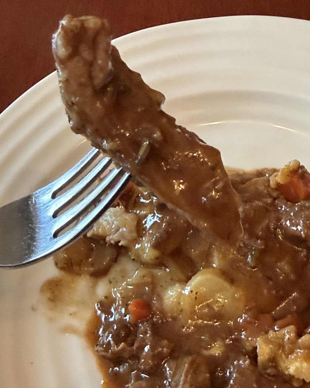 Image of a fork with a piece of steak on it hovering over a plate of steak and ale potato bake.
