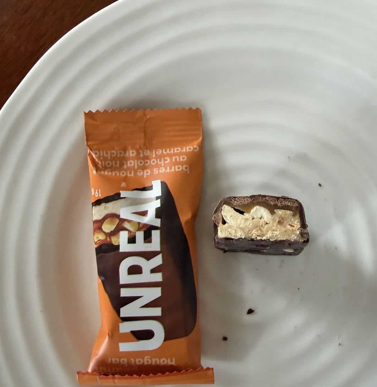 Image of the Costco Unreal Dark Chocolate Peanut Nougat Bar unwrapped standing up beside a wrapped bar on a white plate.