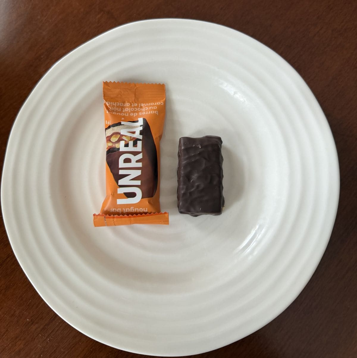 Top down image of a dark chocolate peanut nougat bar in a wrapped beside an unwrapped one.