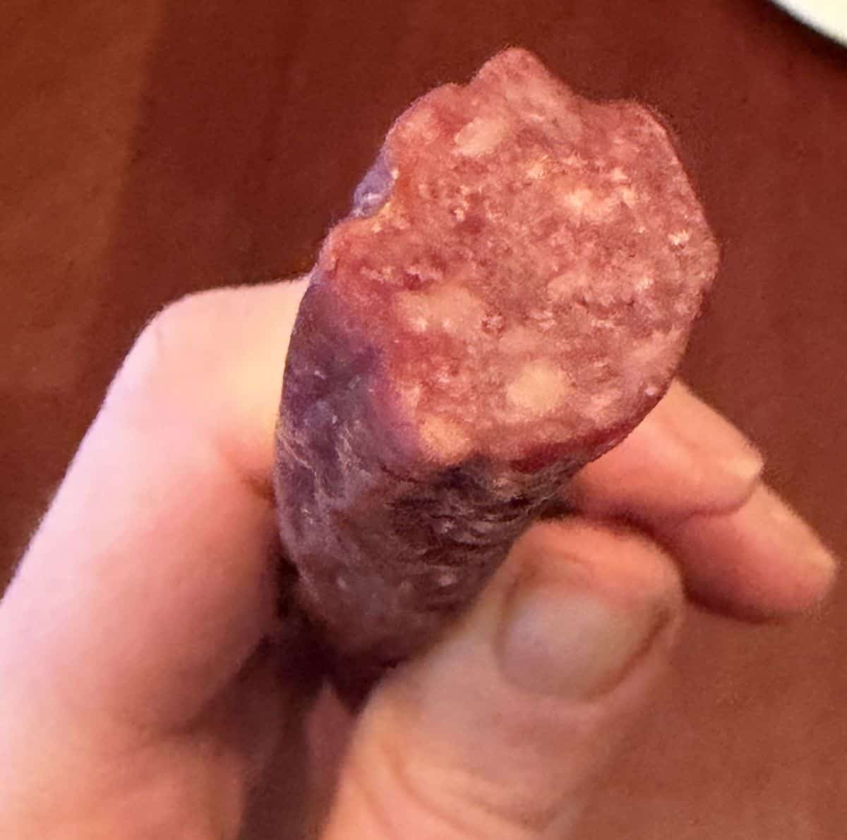 Closeup image of a hand holding one beef stick close to the camera so you can see what the inside looks like.