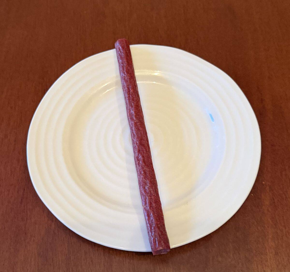 Image of one unwrapped beef stick served on a white plate.