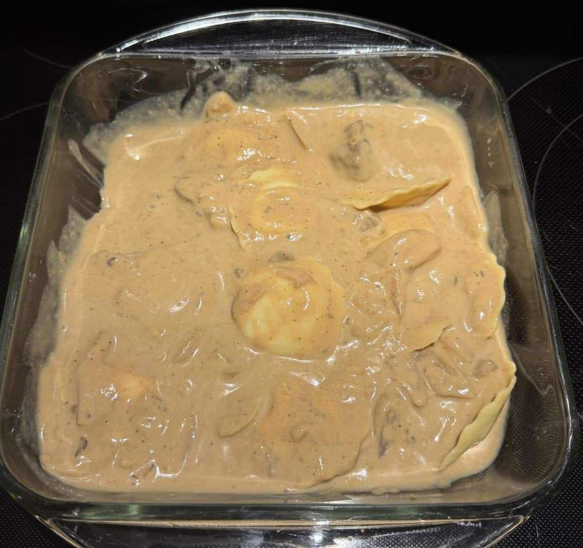 Image of the ravioli and sauce in a glass baking dish before going in the oven.