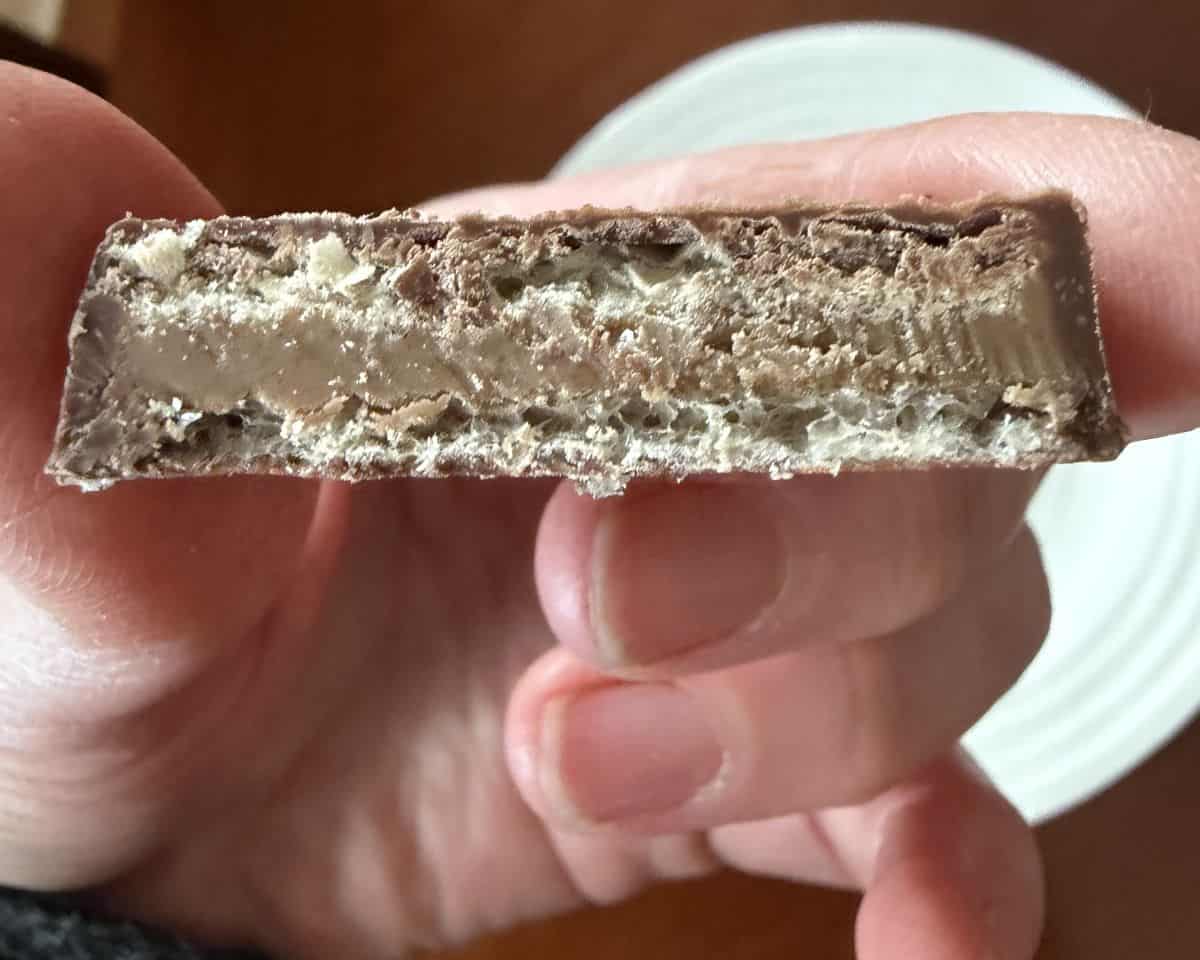 Image of a hand holding one Loacker Tortina Mini with a bite taken out of it so you can see the hazelnut filling.