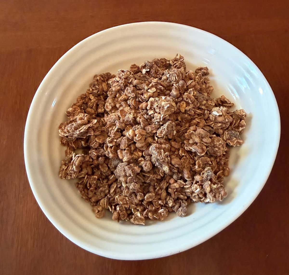 Top down closeup image of a white bowl with granola served in it, sitting on a table.