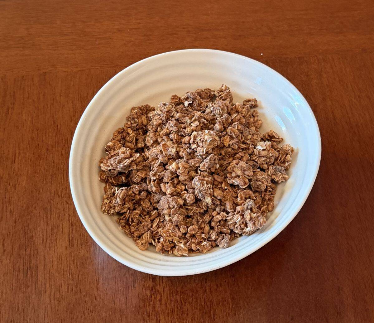 Top down image of a white bowl with granola in it sitting on a table.