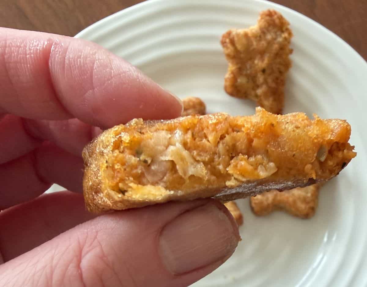 Image of a hand holding one pizza star with a bite taken out of it close to the camera.