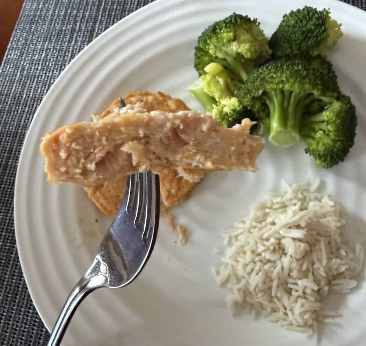 Image of a fork with a piece of a salmon burger on the fork hovering over a plate