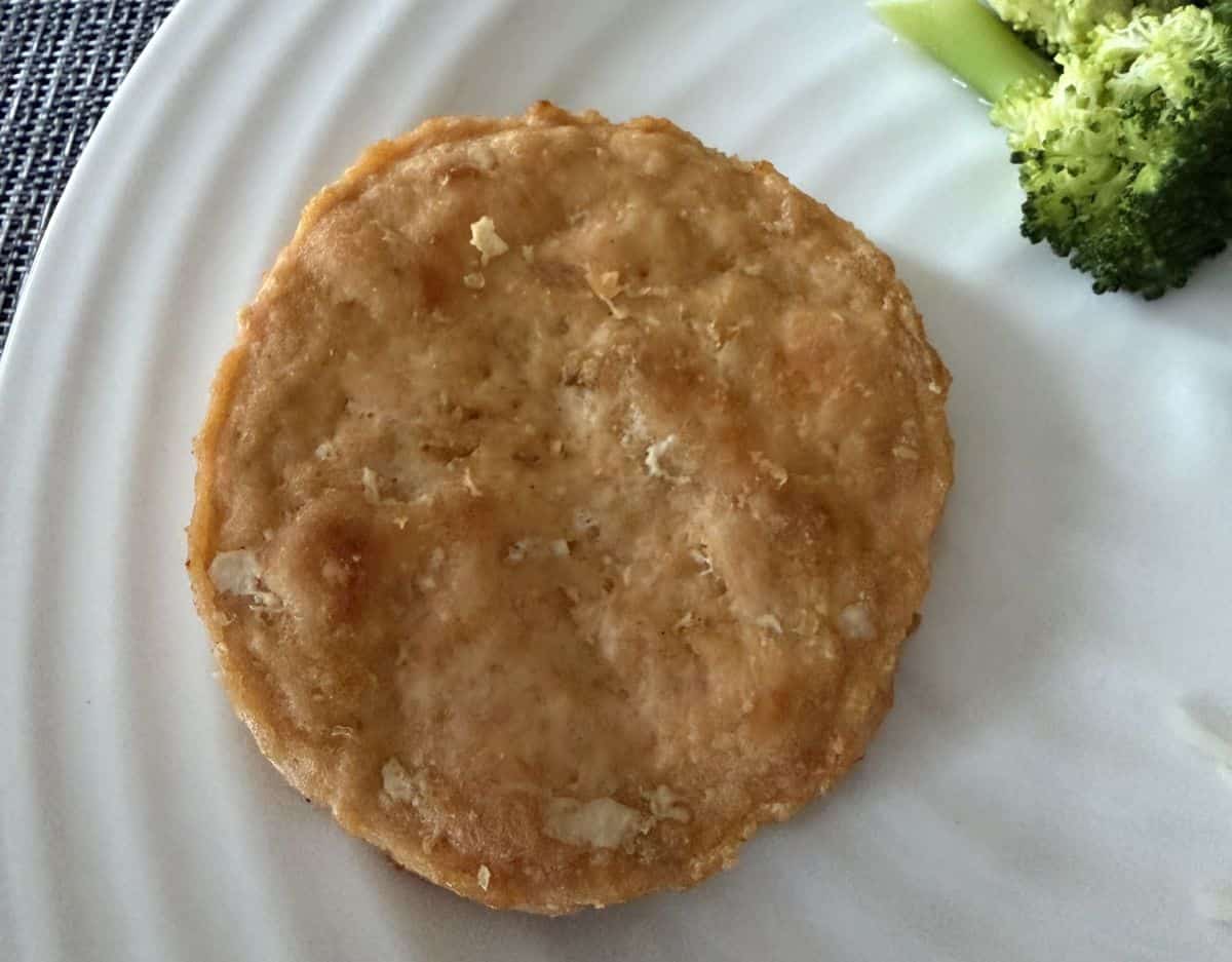Top down image of one cooked salmon burger served on a white plate.
