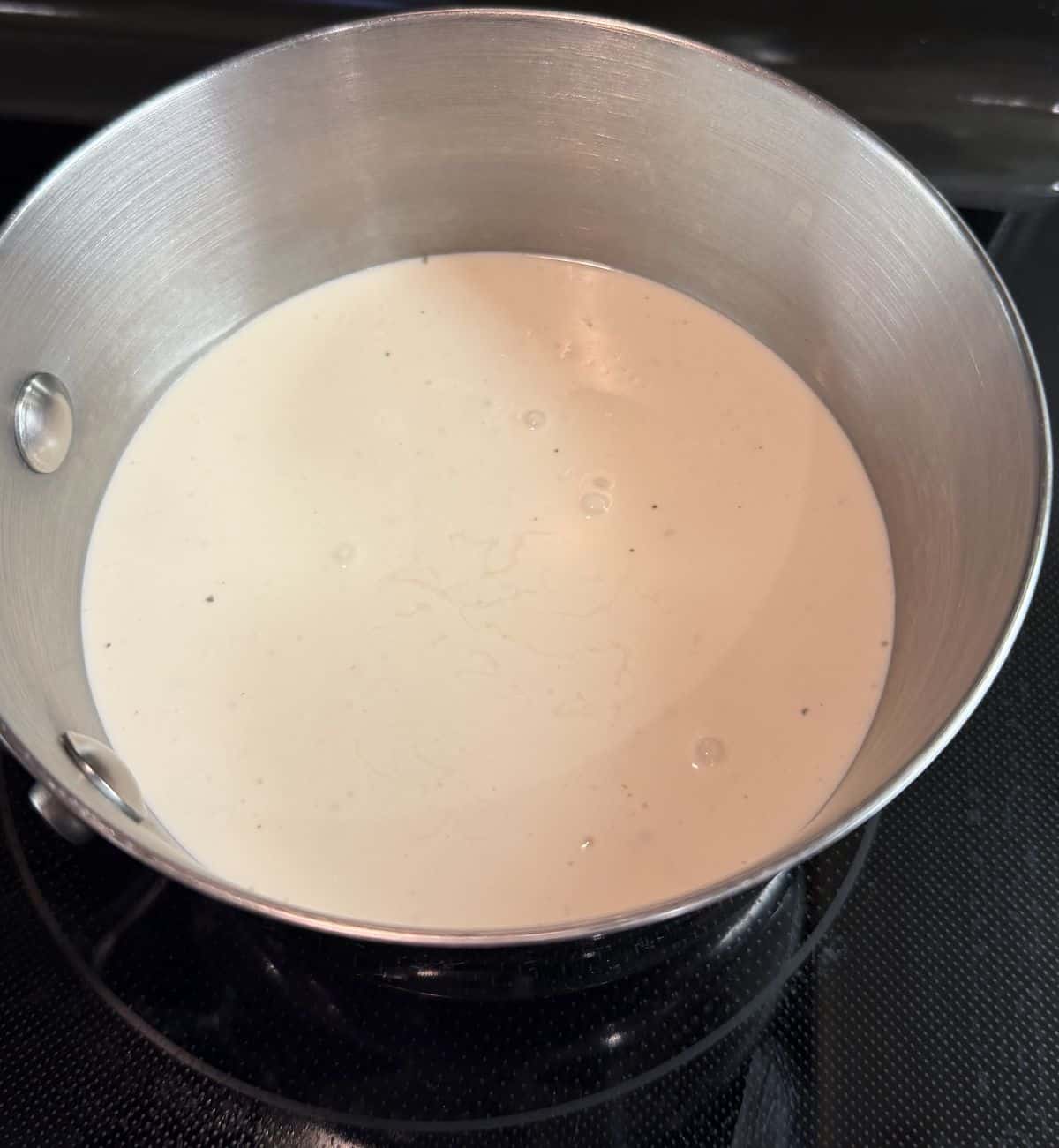 Top down image of the Alfredo sauce being heated in a saucepan on the stove.