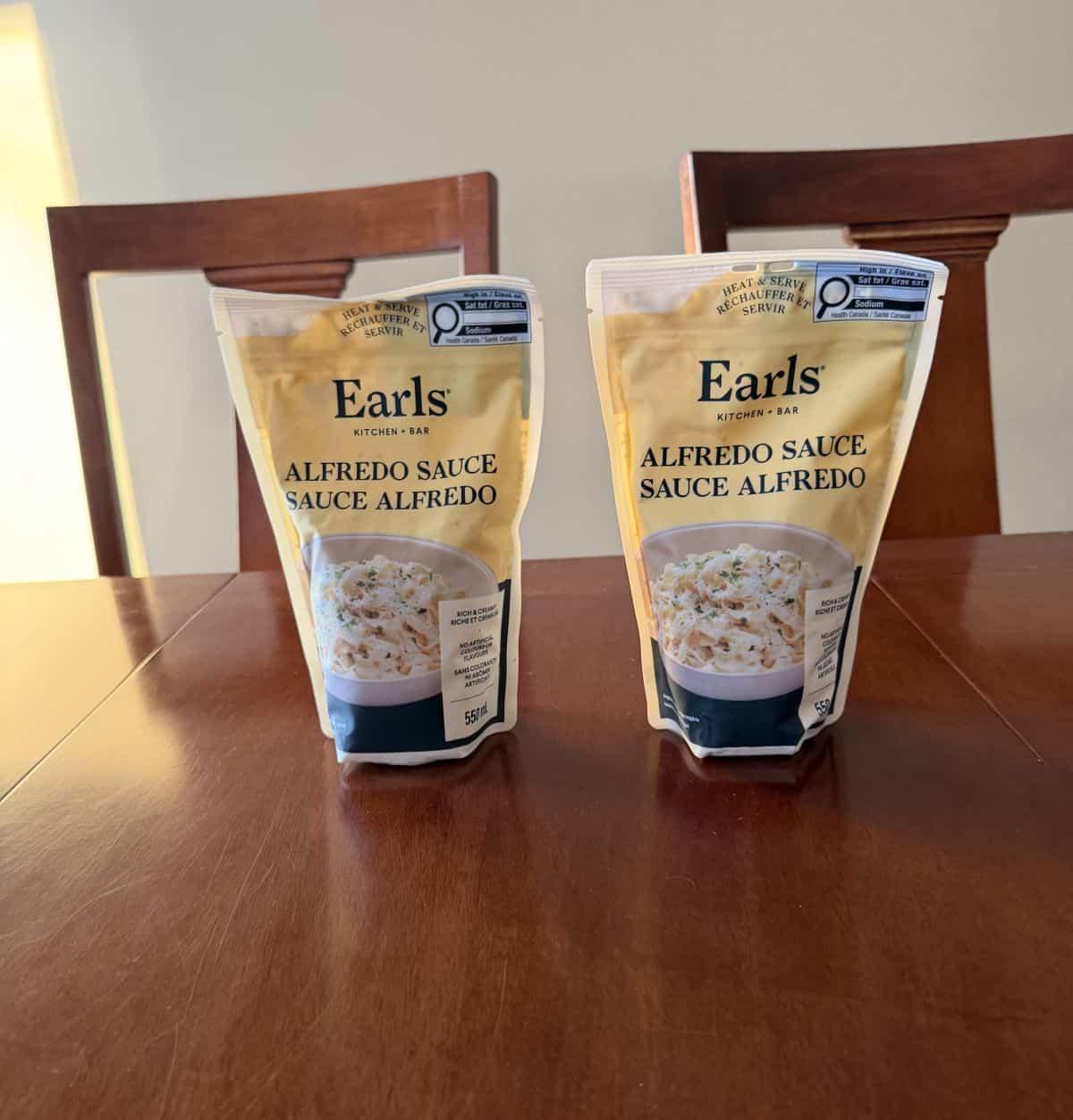 Image of the two packs of Earls Alfredo Sauce side by side unopened on a table. 