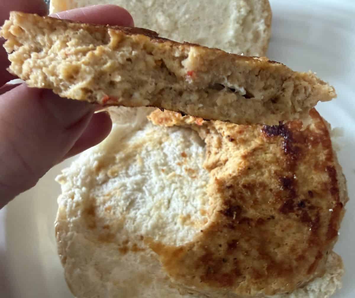 Image of a hand holding a piece of the chicken burger so you can see the inside of the chicken burger.