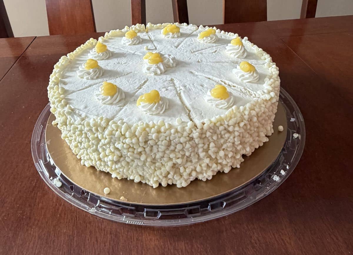 Top-down, side view image of the entire lemon mascarpone cake, you can see scores on the top of the cake indicating where to slice.