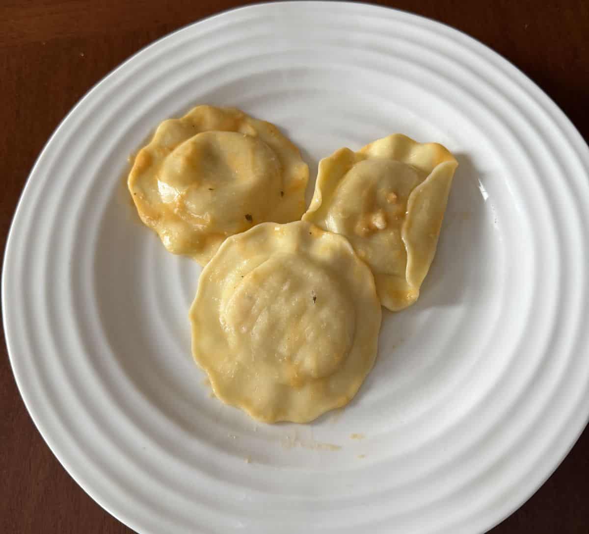 Top-down image of three ravioli cooked and served on a white plate with lobster sauce on top.