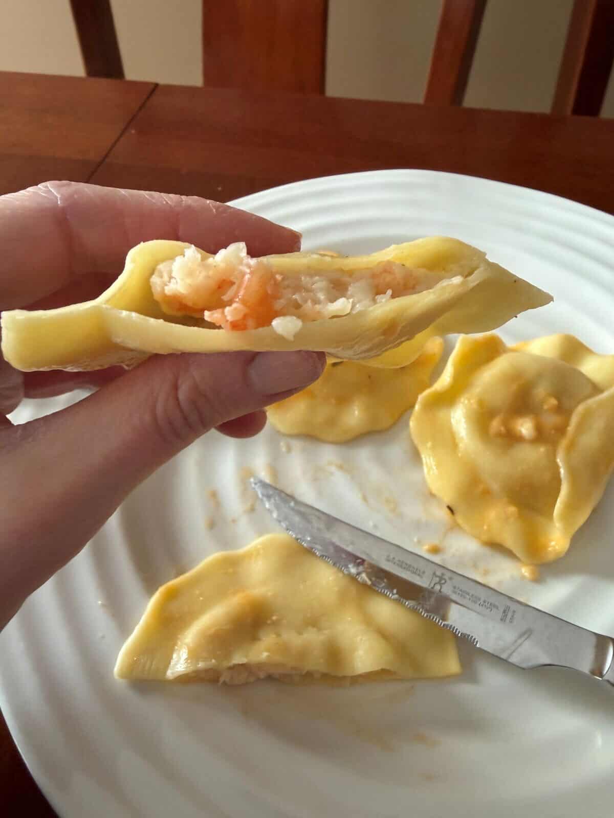 Image of a hand holding one ravioli close to the camera that's been cut in half so you can see the shrimp filling in it.