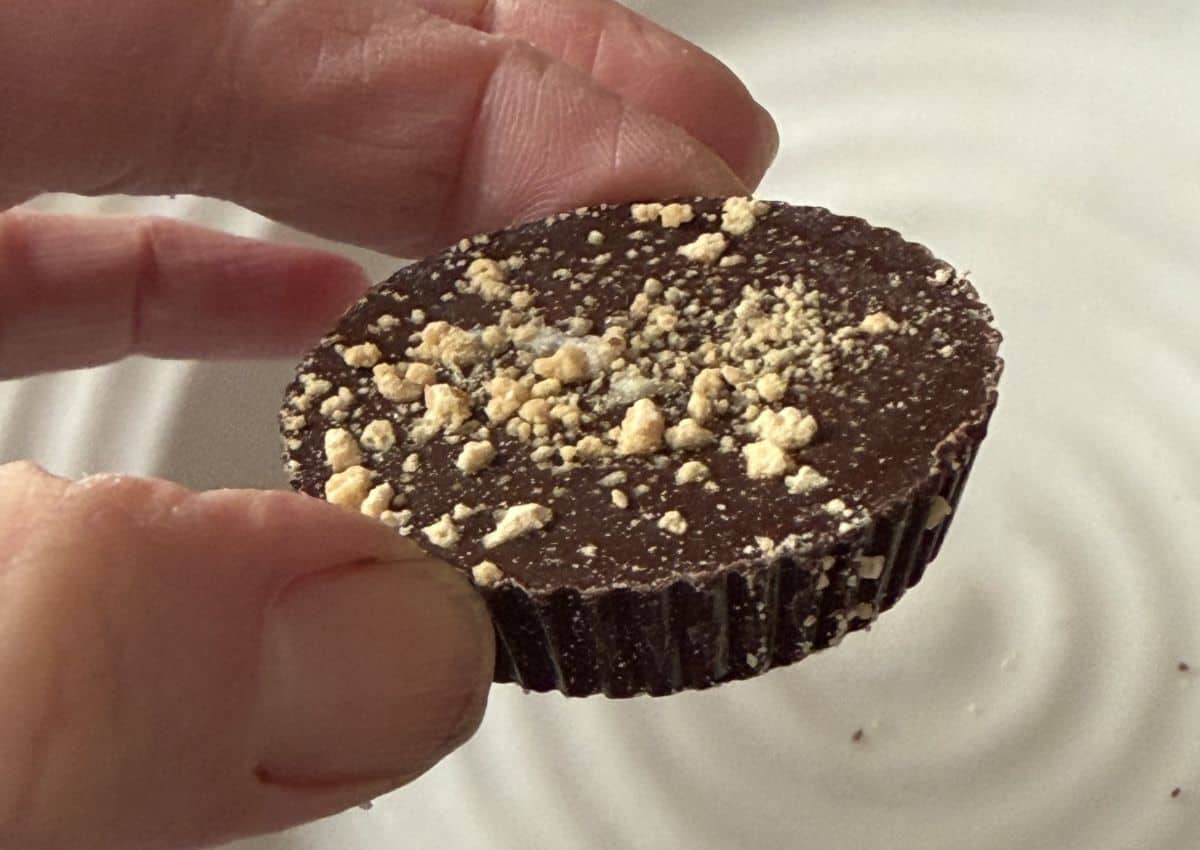 Image of a hand holding one chocolate cup close to the camera hovering over a plate.