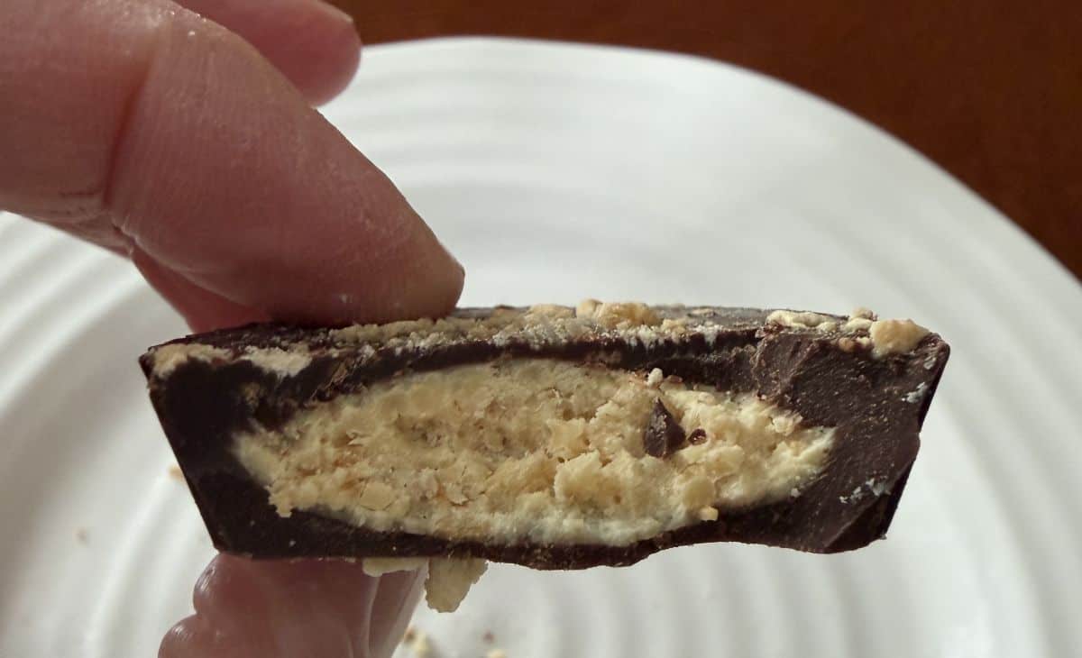 Image of a hand holding one cookie cup with a bite taken out of it so you can see the filling.