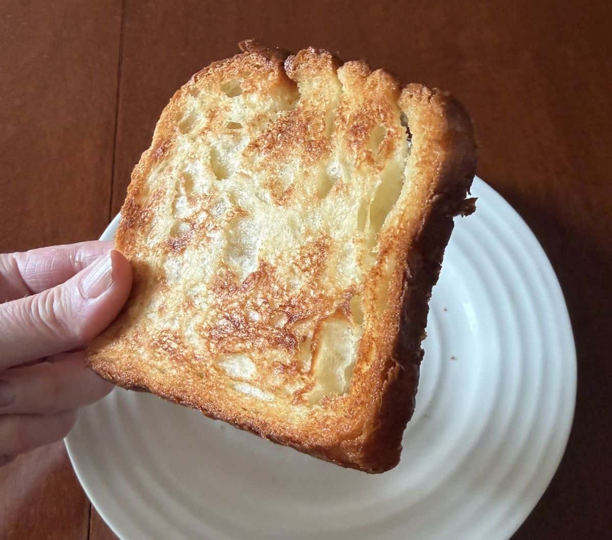 Image of a hand holding one slice of croissant loaf that's been toasted on it's side close to the camera. 