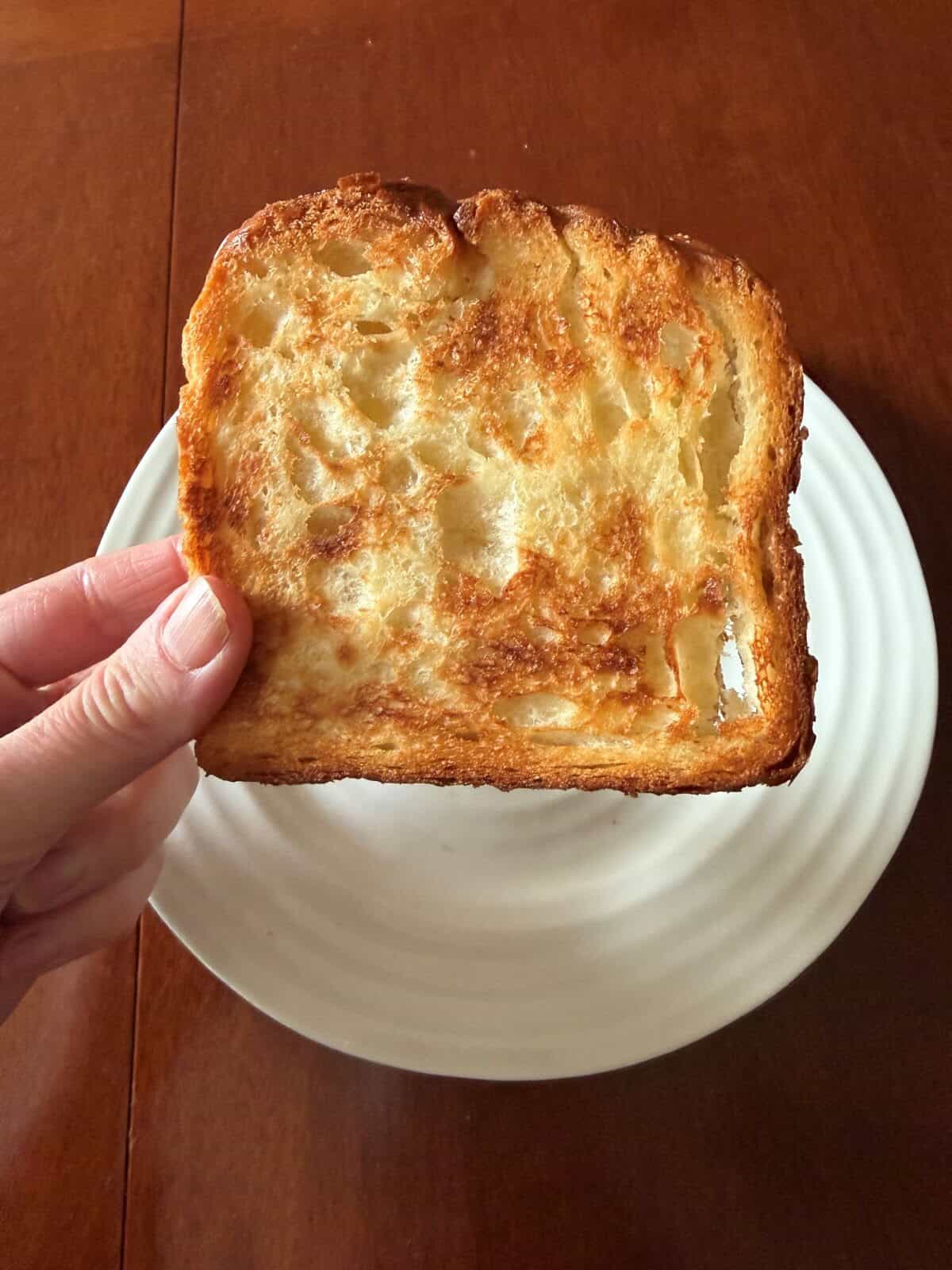 Image of a hand holding one slice of the croissant loaf, toasted, close to the camera. 