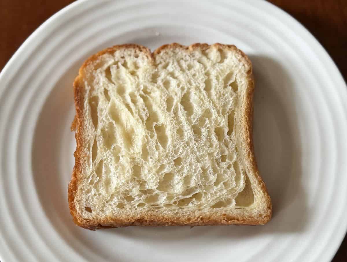 Image of one slice of untoasted croissant loaf served on a white plate. 