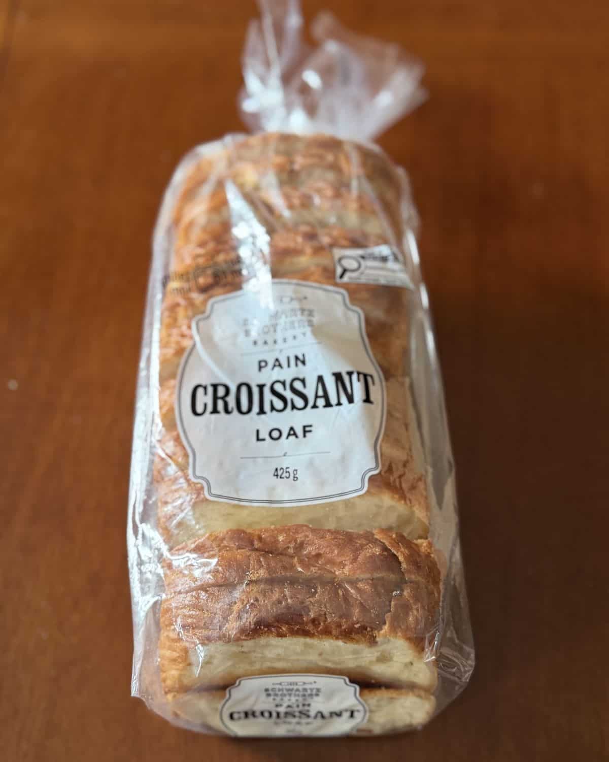Image of one croissant loaf sitting on a table unopened. 