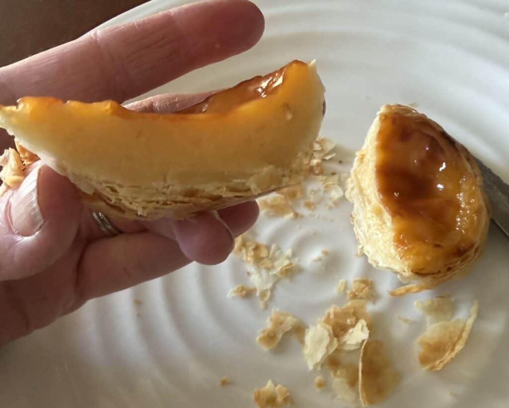 Image of a hand holding one tart that's been cut in half close to the camera so you can see the custard filling.