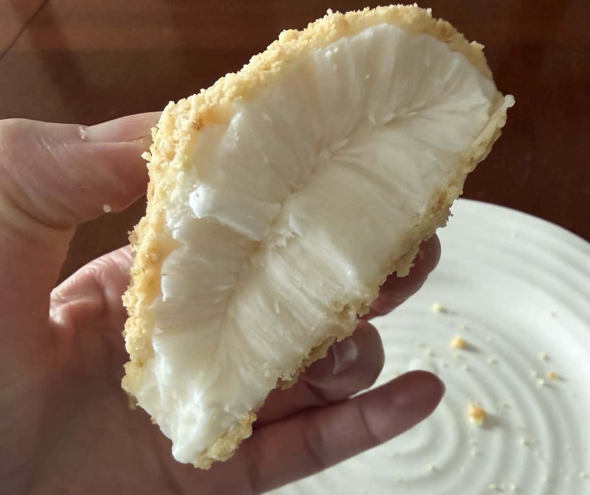 Image of a hand holding one drumstick dessert with a few bites taken out of it close to the camera so you can see the filling.