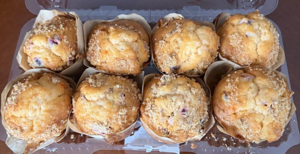 Top-down image of a pack of eight cranberry orange muffins with the lid off so you can see the top of the muffins.