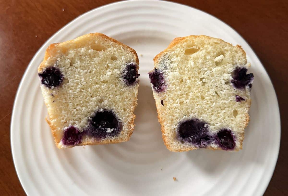 Image of one blueberry muffin cut in half and served on a plate so you can see the inside of the muffin.