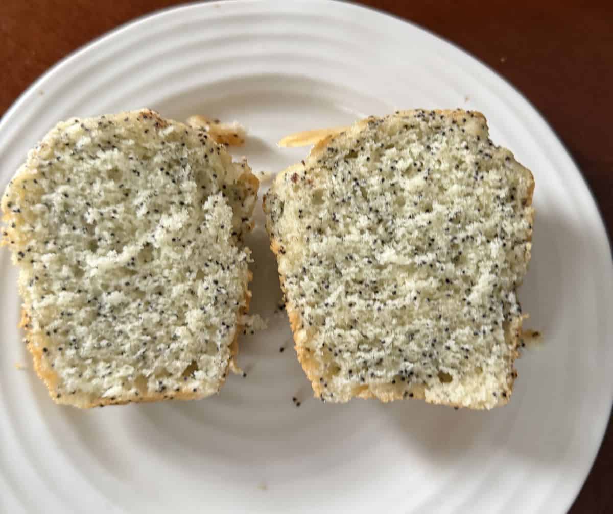 Image of one almond poppy seed muffin cut in half and served on a white plate so you can see the inside of the muffin.