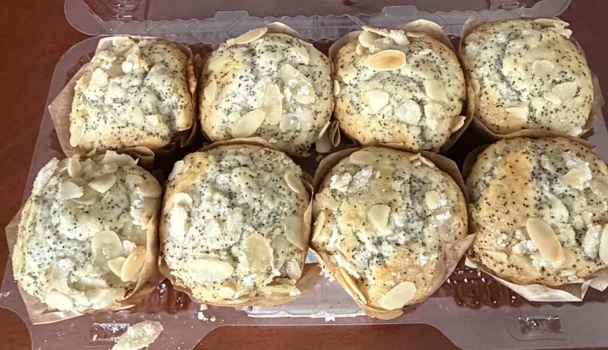 Top-down image of a pack of eight almond poppy seed muffins with the lid off so you can see the top of the muffins.