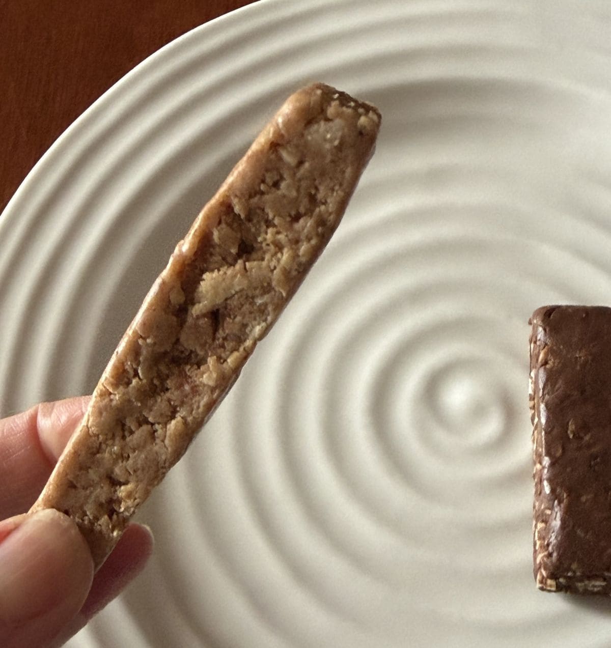 Image of a hand holding one peanut butter chocolate chip Mush bar so you can see what the side of the bar looks like.