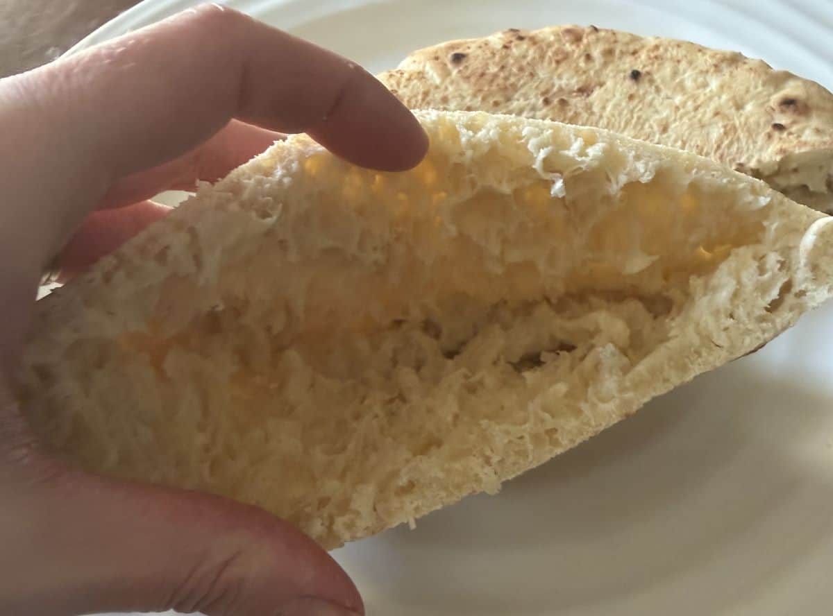Image of a hand opening half of a pita to show what the pita looks like inside.