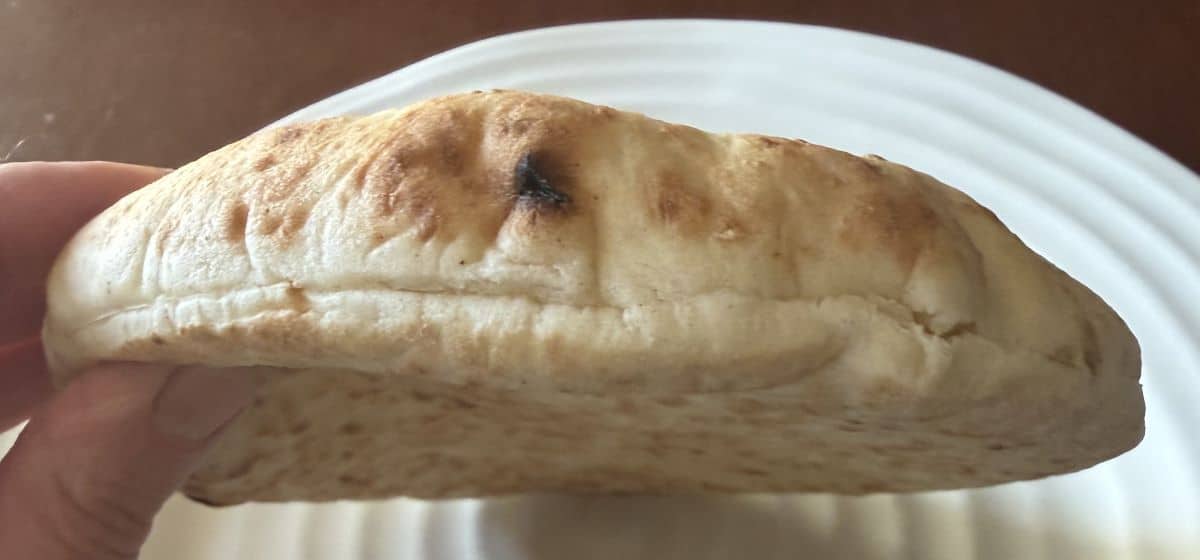 Image of a hand holding one pita bread close to the camera so you can see how thick it is.